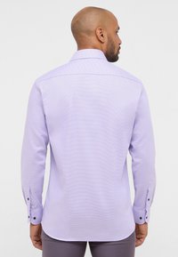 Camicia lunga a maniche viola chiaro con un sottile motivo a quadri, orlo arrotondato e polsini con bottoni che presentano dettagli in bottone nero. Vista posteriore mostrata.