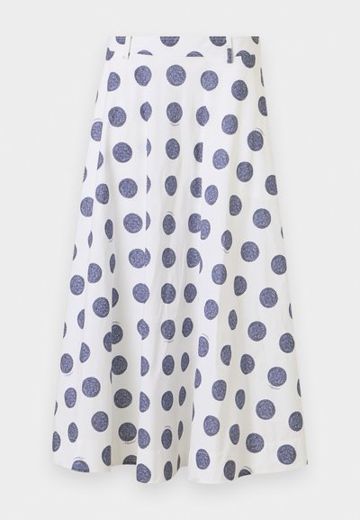 En knælængde, hvid nederdel med en udvidet design, der har store marineblå polkaprikker. Den har en glat tekstur og plisserede detaljer.