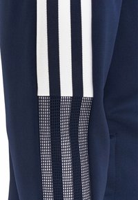 Mallas deportivas azul marino con un panel lateral de malla texturizada, tres franjas verticales blancas y un acabado de tejido suave.