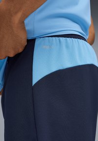 Des shorts de sport bleus avec une texture en mesh comportent un panneau marine et un logo "DRYCELL" en argent. Le design combine la fonctionnalité d'évacuation de l'humidité.