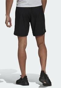 Zwarte sportshorts met een losse pasvorm, een gladde textuur, en een subtiele logo-detail op de zoom, gecombineerd met zwarte sportschoenen.