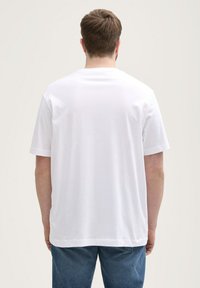 Camiseta blanca de algodón, de manga corta, corte relajado, vista posterior. Detalles de costura y una textura suave, combinada con jeans de mezclilla azul.
