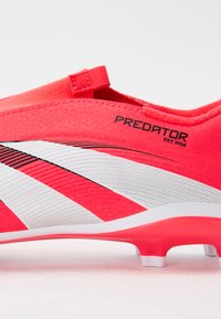Les chaussures de football rose vif présentent un upper texturé, des rayures diagonales blanches et noires, et une semelle arrondie avec des crampons moulés pour une traction optimale.