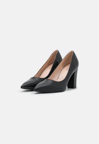 Tacones altos de cuero negro con punta afilada y tacón grueso. El interior es de un color claro, lo que realza el diseño elegante.