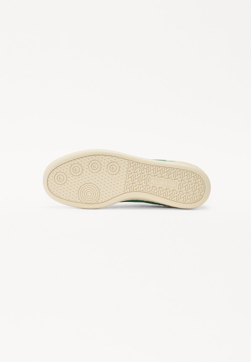 Suola verde di una sneaker con una superficie in gomma beige testurizzata caratterizzata da motivi circolari e scanalature lineari per una presa ottimale.