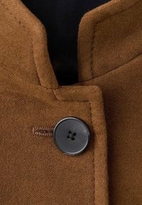 Gros plan sur le col d'un manteau en laine marron avec un grand bouton noir à quatre trous fixé à travers une boutonnière cousue.