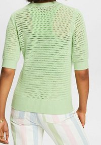 Miętowy sweter dzianinowy z krótkimi rękawami, z otwartym splotem i ribbowanymi mankietami oraz dołem, noszony z paskowanymi, pastelowymi spodniami.