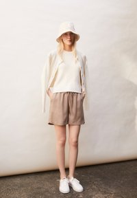 Cream ribbed sweater and beige shorts, paired with a light beige bucket hat and white sneakers, against a neutral backdrop.