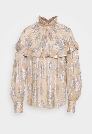 Blouse beige à manches longues avec col haut à volants, motif floral argenté et détail à volants sur la poitrine et le haut des bras.