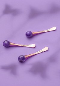 Tre rulli facciali in cristallo viola con manico in oro rosa, caratterizzati da un design sfaccettato e testo incisa "CRYSTALLOVE", su uno sfondo lavanda.