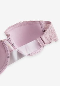 Jasnoróżowy biustonosz z koronkowymi dodatkami, gładką tkaniną, regulowanymi ramiączkami, falistymi krawędziami i subtelnym logo na taśmie.