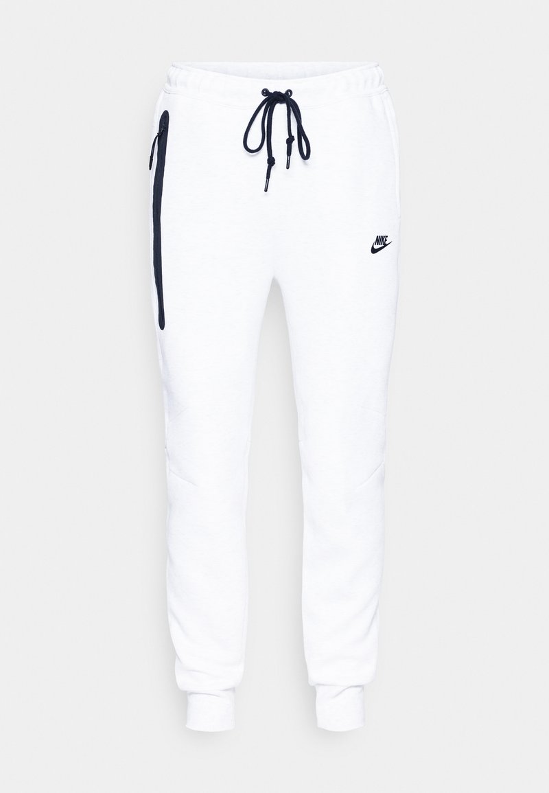 Pantalones jogger de felpa blanca con cintura ajustable mediante cordón, bolsillos laterales con cremallera, puños acanalados y un logotipo negro de Nike en el muslo izquierdo.