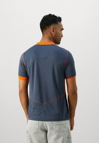 Chemise à manches courtes pour homme en gris foncé avec des accents et des coutures orange. Elle présente une texture en maille et un col rond.