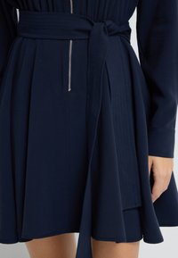 Granatowa sukienka z teksturowanej tkaniny, plisowanym dołem i paskiem w talii z zamkiem z przodu.