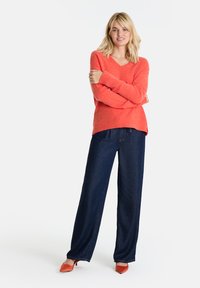 Koralle V-Ausschnitt Pullover aus weichem Stoff, kombiniert mit dunkelblauen weiten Jeans und orangefarbenen spitzen Absätzen, mit lässiger, entspannter Passform.