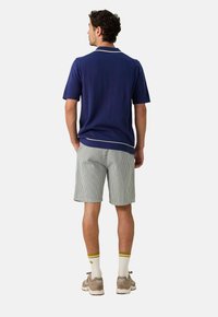 Marineblauwe polo met korte mouwen en witte bies, gecombineerd met grijs-witte gestreepte shorts. Sportieve schoenen en sokken met gele strepen.