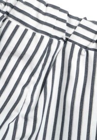 Tessuto di cotone con strisce verticali blu navy e bianche, dotato di una vita arricciata e di una sottile texture. Dettagli della pattina su misura visibili.