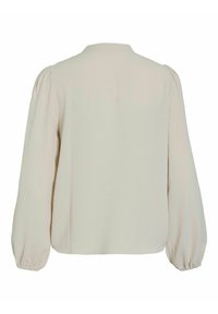 Blusa color crema con scollo rotondo, maniche lunghe a palloncino e polsini arricciati. Realizzata in tessuto leggero con una texture liscia.
