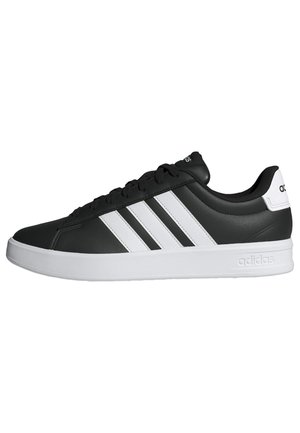 Zapatilla Adidas negra de corte bajo con suela blanca, tres rayas laterales blancas y marca Adidas en el talón y la lengüeta.