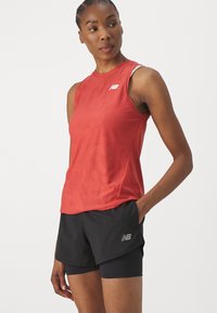 Red sleeveless athletic top with textured pattern and white logo, paired with black shorts. Both garments designed for performance and movement.