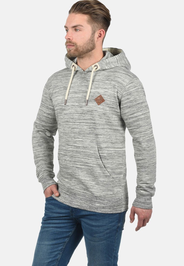 Gray, textured hoodie with a kangaroo pocket, adjustable drawstring, and a small brown logo patch on the chest. Worn with blue jeans.
