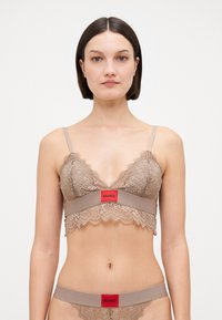 Lace bralette i beige med vågiga kanter och ett röd logoband. Den delikata texturen och de justerbara axelbanden fulländar designen.