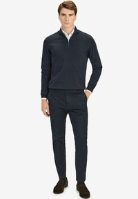 Tummansininen neule, jossa on neljänneksen vetoketju, valmistettu pehmeästä materiaalista. Yhdistettynä tummiin housuihin ja ruskeisiin samettikenkiin, luoden siistin ilmeen.