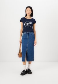 Marine t-skjorte med grafikk foran, parret med et blått denimskjørt med frontspalte, og svarte platåsko med hvite sokker.