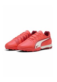 Chaussures de football synthétiques rouges au design élégant, avec un dessus texturé, un système de laçage détaillé et des accents blancs contrastants sur les côtés.