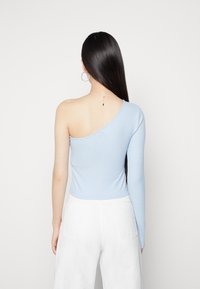 Světle modrý žebrovaný top s dlouhými rukávy a odhaleným jedním ramenem, těsný střih, spojený s bílými kalhotami vysokého pasu.