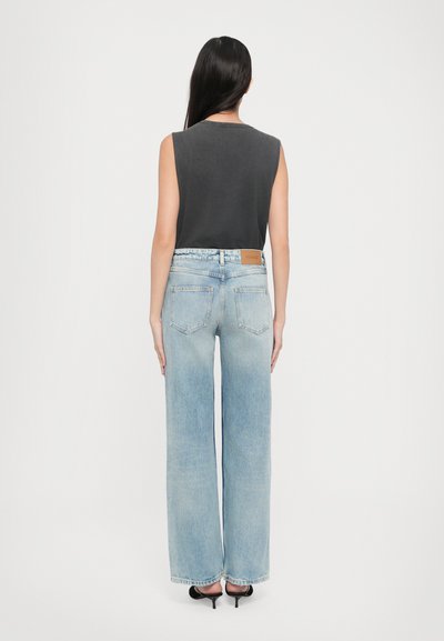 Mouwloos grijs topje met een ronde hals, gecombineerd met lichtblauwe wijde jeans met een leren label aan de achterkant en een minimalistisch ontwerp.