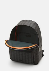 Rucsac negru cu un model geometric, interior portocaliu și verde, compartiment cu fermoar, bretele ajustabile și bază solidă.