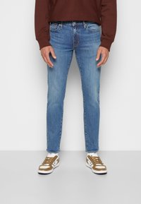 Ljusblå jeans med en smal passform, med urtvättade områden och en klassisk femfickorsdesign. Matchas med bruna och vita sneakers.