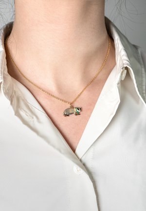 Gold chain necklace featuring a detailed badger pendant with grey and black enamel accents against a white shirt.