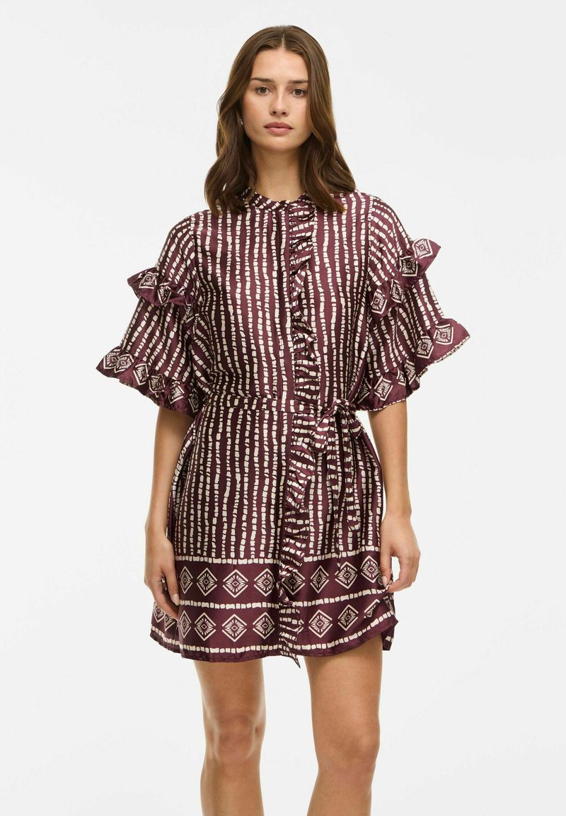 Vestito bordeaux con motivi geometrici bianchi, maniche a volant, chiusura con bottoni e vita legata, realizzato in un tessuto morbido e leggero.