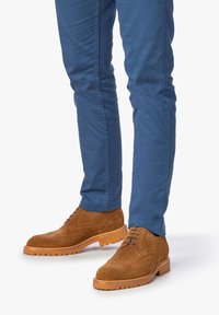 Zapatos brogue de ante marrón con detalles perforados, suela de goma color marrón, combinados con pantalones slim fit azul.