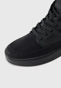 Baskets montantes noires en cuir texturé avec une finition lisse. Présentent des lacets plats, un col rembourré et un logo en relief sur le côté.