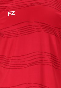 Punainen urheiluhaalari, jossa on tekstuuripinta vaakasuorista viivoista. "FZ"-logo valkoisena vasemmalla puolella. Sileä kangasviimeistely.