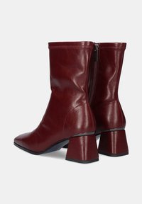 Botas de cuero burdeos hasta el tobillo con punta afilada, tacón bloque de altura media, cremallera lateral y textura suave. Diseño sencillo sin adornos.