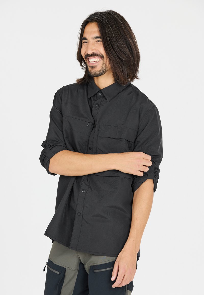 Zwarte langemouwen shirt met twee voorzakken, knoopkraag en opgerolde mouwen. Gladde stofstructuur met subtiele patroondetails.