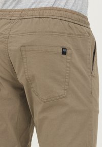 Pantalon en coton beige avec une taille élastique, des poches latérales et une poche arrière ornée d'une petite étiquette logo. Tissu texturé avec une finition durable.