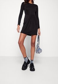 Robe noire à manches longues avec un design drapé, assortie à des chaussures à plateforme noires, des chaussettes bleues scintillantes et un petit sac à main bleu.