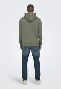 Oliven grøn hættetrøje med en afslappet pasform, ribbede ærmer og kant, kombineret med blå denim jeans og hvide sneakers.