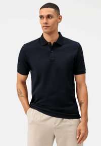 Kurzärmeliges Navy-Polohemd in einfarbiger Ausführung, mit einer Drei-Knopf-Leiste und einer glatten Stoffstruktur. Getragen mit hellen Hosen.