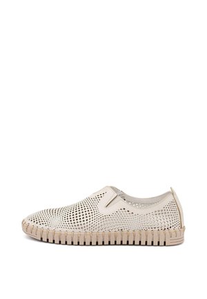 Zapato beige tipo mocasín con parte superior perforada, paneles laterales elásticos y suela flexible texturizada para transpirabilidad y comodidad.