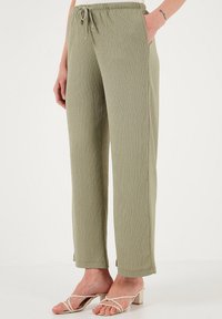 Pantalons en tissu texturé vert clair avec une taille élastique et un détail de cordon de serrage. Conception à jambes droites avec poches latérales.