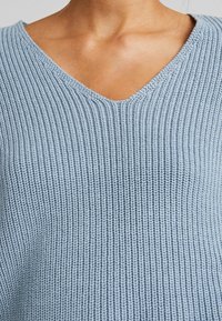 Maglione lavorato a maglia di colore azzurro chiaro con scollo a V, texture a coste e vestibilità rilassata. Il tessuto mostra cuciture uniformi e un aspetto morbido.