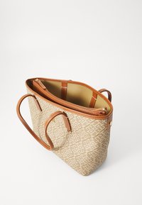 Beige mønstrede totebag med brune læderhåndtag, der har en lynlåslomme indeni og en solid beige foret.