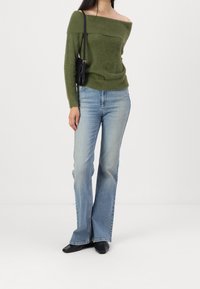 Maglione verde a spalle scoperte, jeans a zampa d'elefante blu chiaro, scarpe nere a punta e una piccola borsa nera. Tessuto morbido e vestibilità casual.