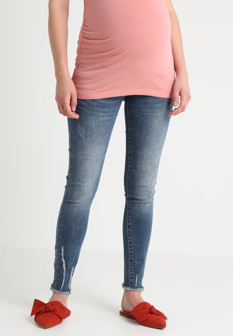 Smala jeans i blekt blå denim med slitna detaljer. Kombinerade med röda mocka slip-on-skor med en rosett. Topp är enfärgad rosa.